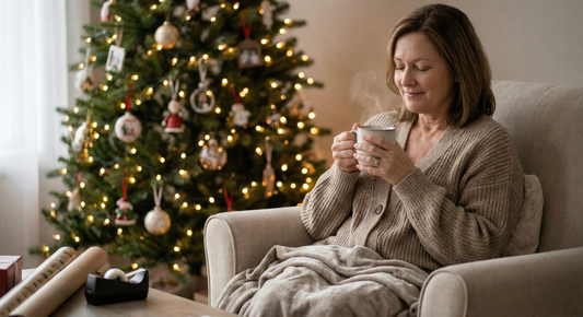 Middle-aged woman relaxing in a cozy armchair with a warm beverage, smiling peacefully in front of a beautifully lit Christmas tree, symbolizing calm, self-care, and holiday mindfulness for women during the festive season.