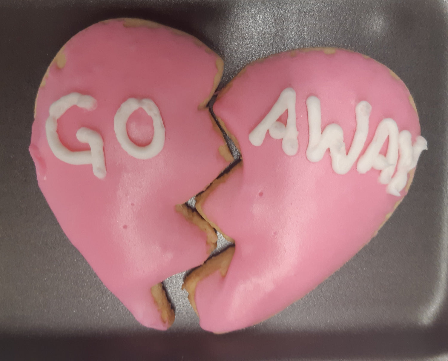 Pink heart-shaped cookie split in half with the words Go Away written in white icing